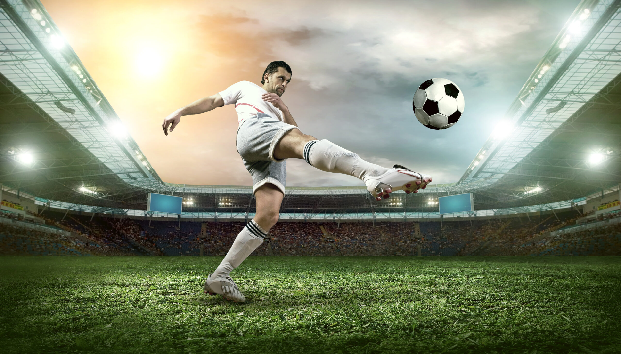 A footballer in a white jersey kicking the ball in the middle of the field.