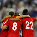 Three football players hugging each other and celebrating scoring a goal.