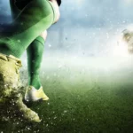 a closeup of footballer's legs in green socks kicking a ball on a football field.