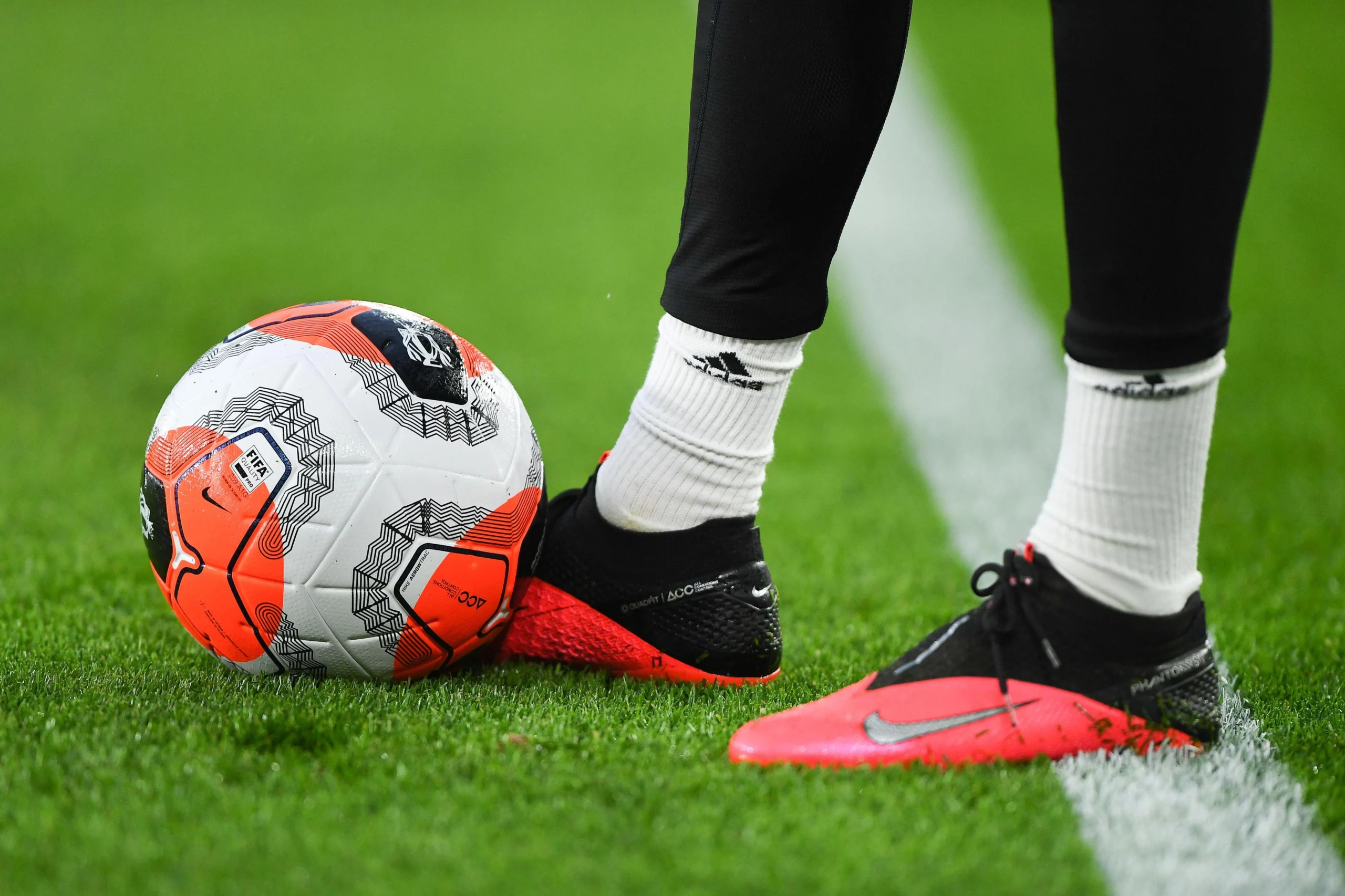 A picture of a football player's boots besides a ball on a football field.